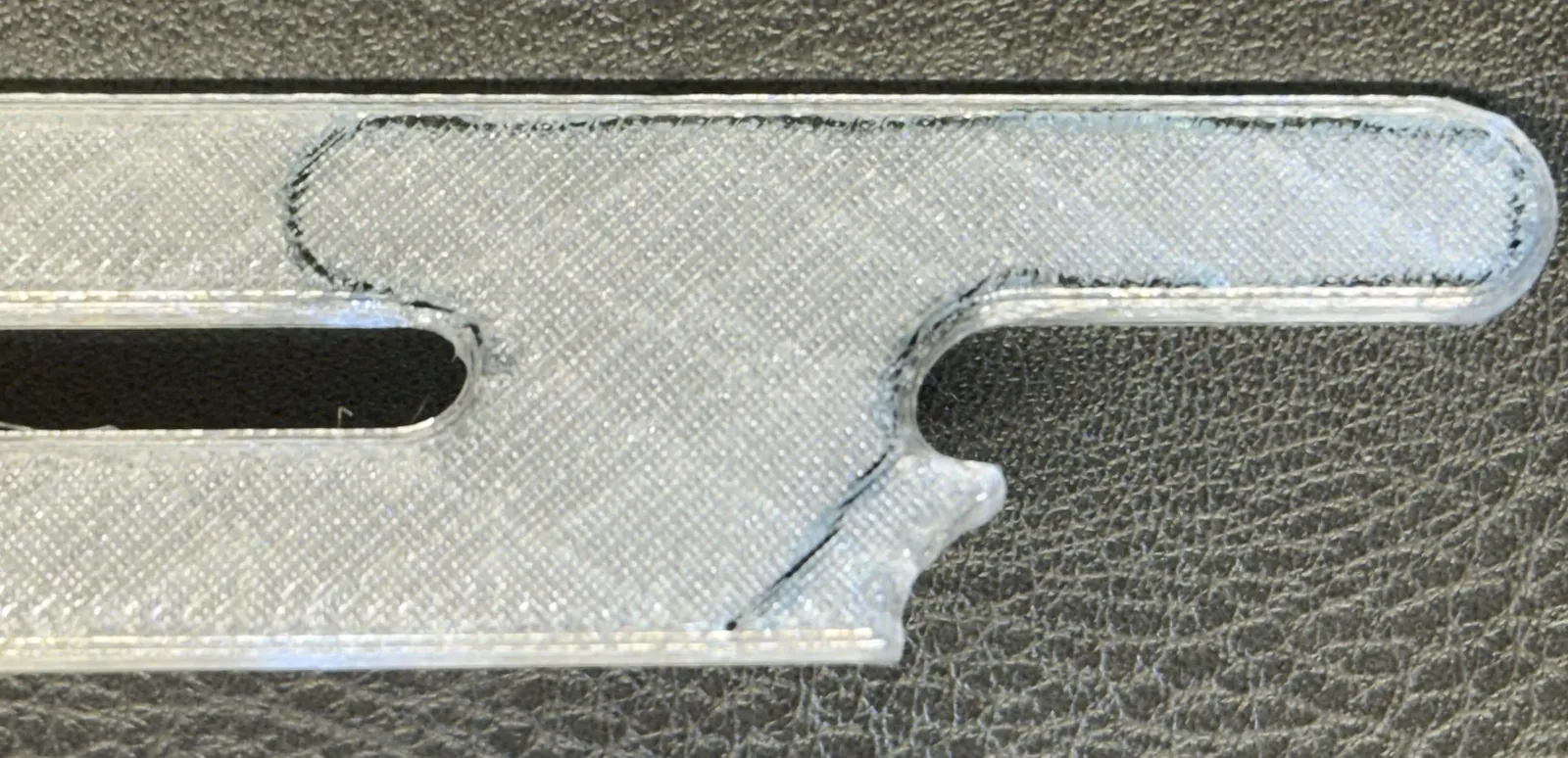 Photo of the printed opener in clear polymer on dark leather. A thin dark line of continuous fiber runs inside it along the jaw, throat and roof.